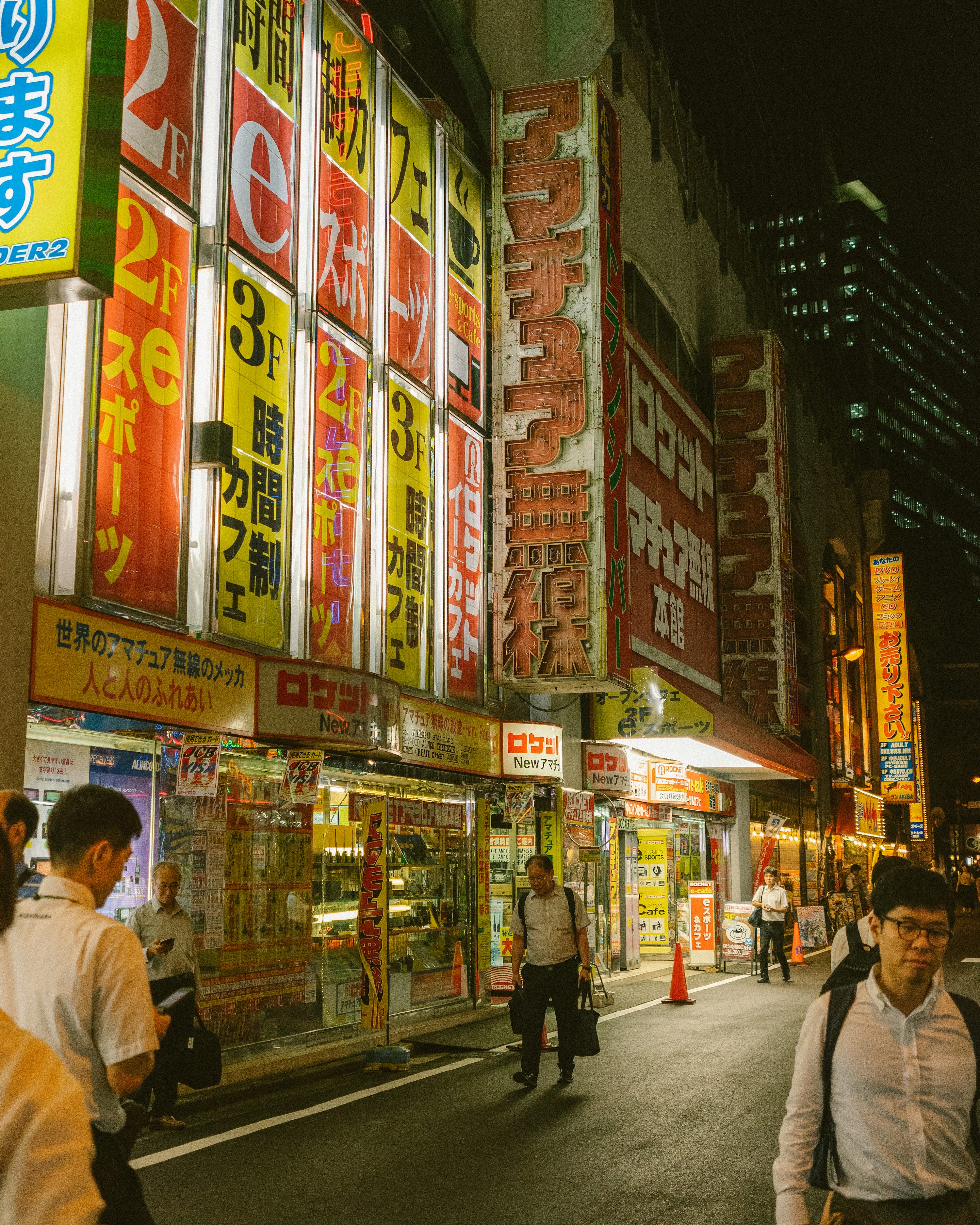 Illuminated electronics shops and pedestrians in Akihabara, Tokyo, at night.